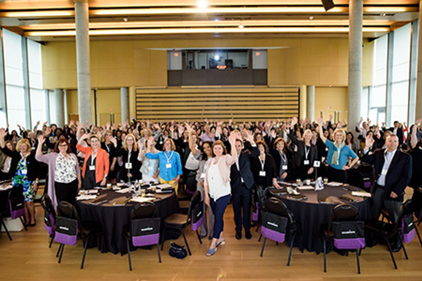 Large crowd of people stading with arms raised in large conference room