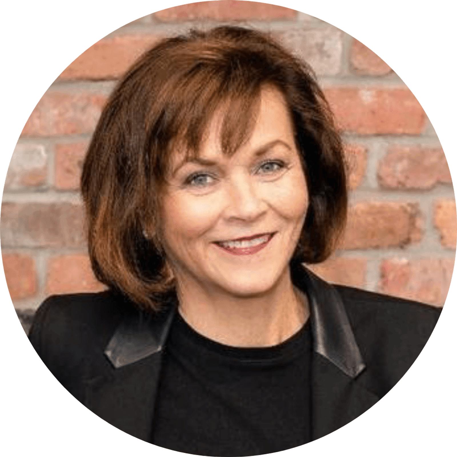 Anne Zacharias' headshot with a brick wall in the background in a circular frame