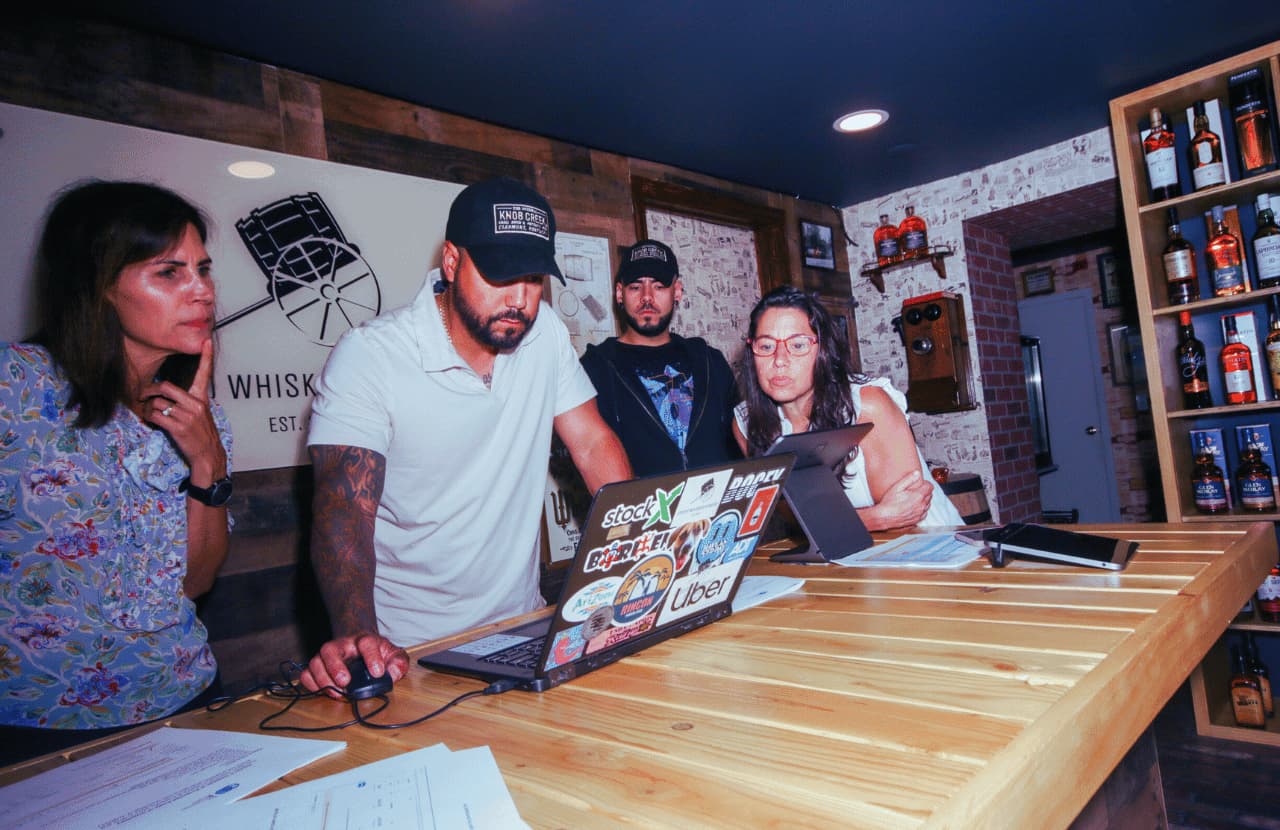 A group of The Acceleration Project consultants gather around a countertop looking at a laptop