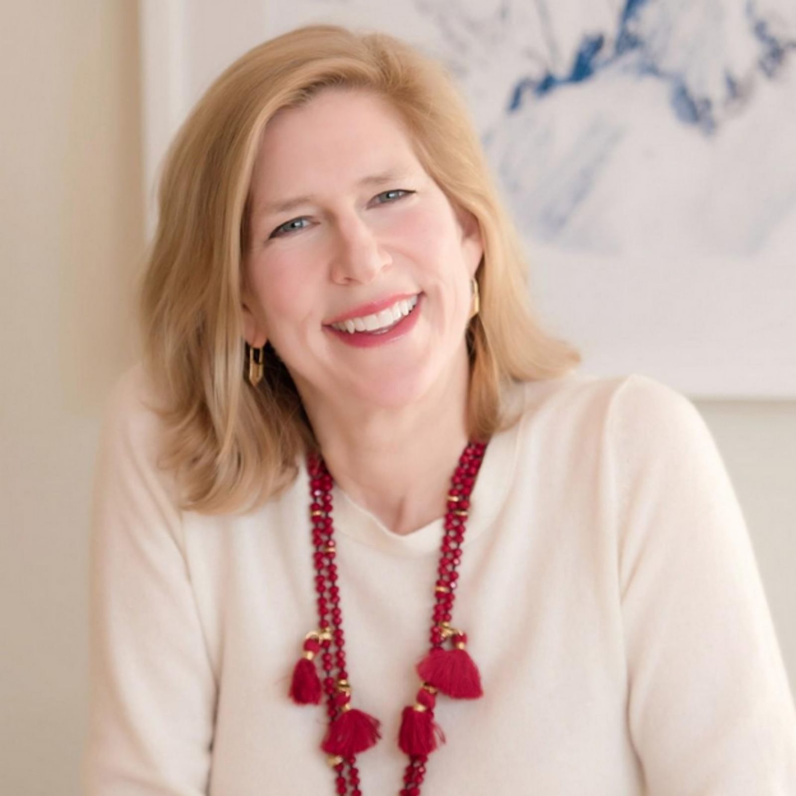 Sara Dickison Taylor smiles in her headshot wearing a white sweater and red necklace