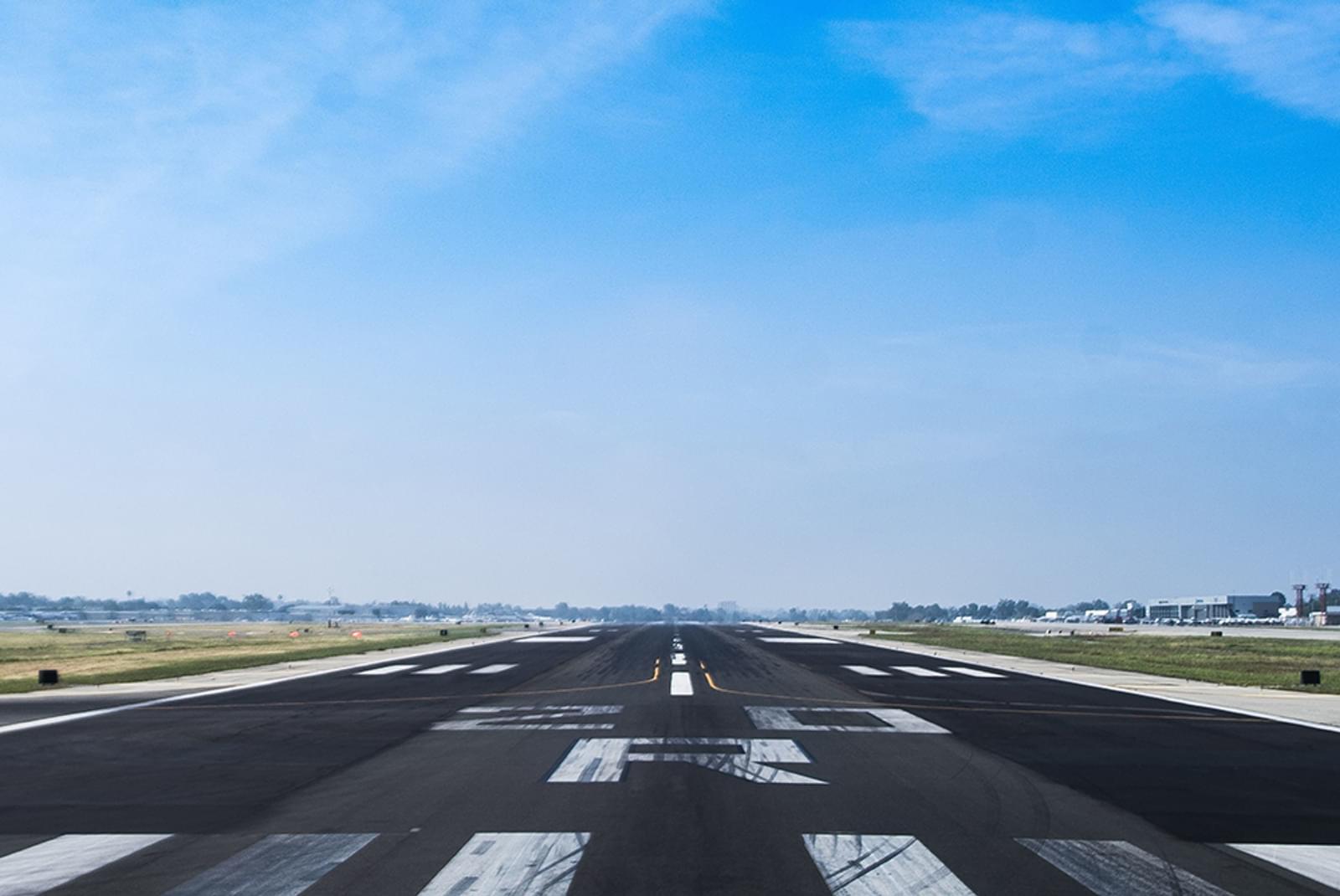 Underneath a bright blue sky, an airplane runway leads off into the horizon, providing a space to land.