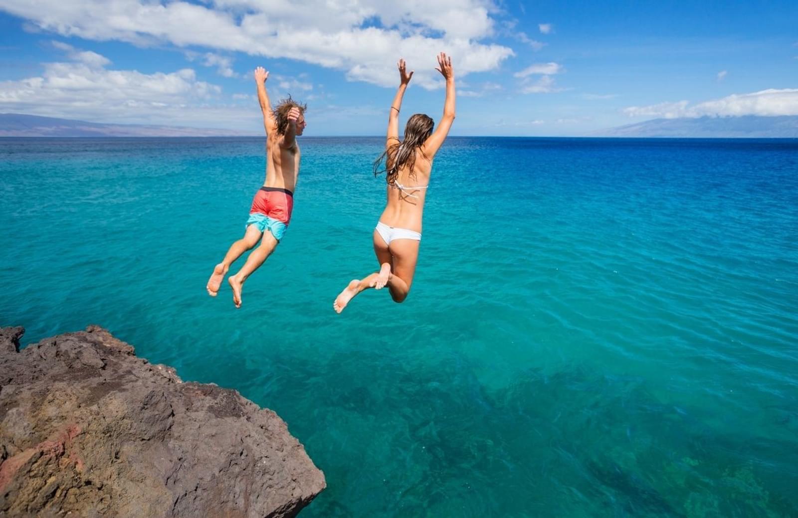 Two girls juping into clear blue ocean water