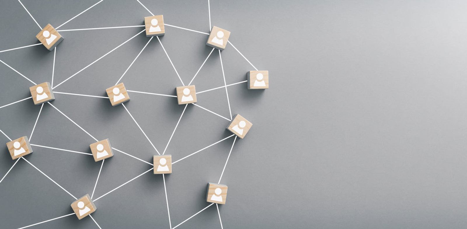 Wooden blocks with icons of people are connected in a network by white lines against a grey backdrop