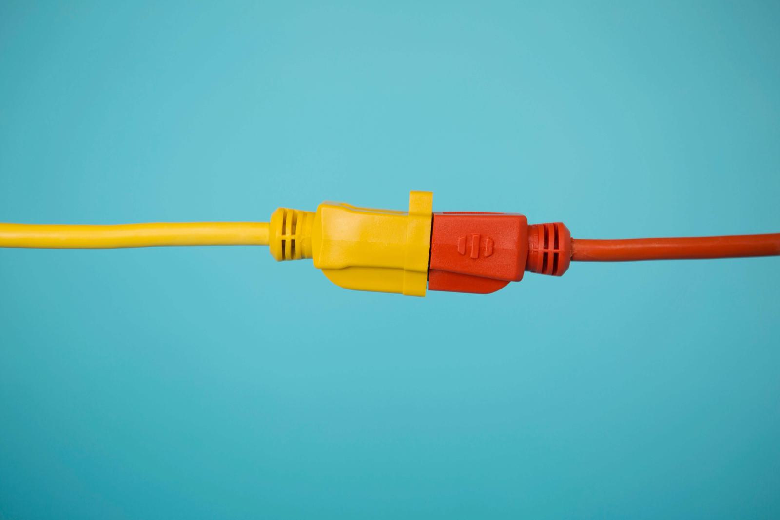 Connected yellow and orange electrical cords plugged into each other against teal backdrop