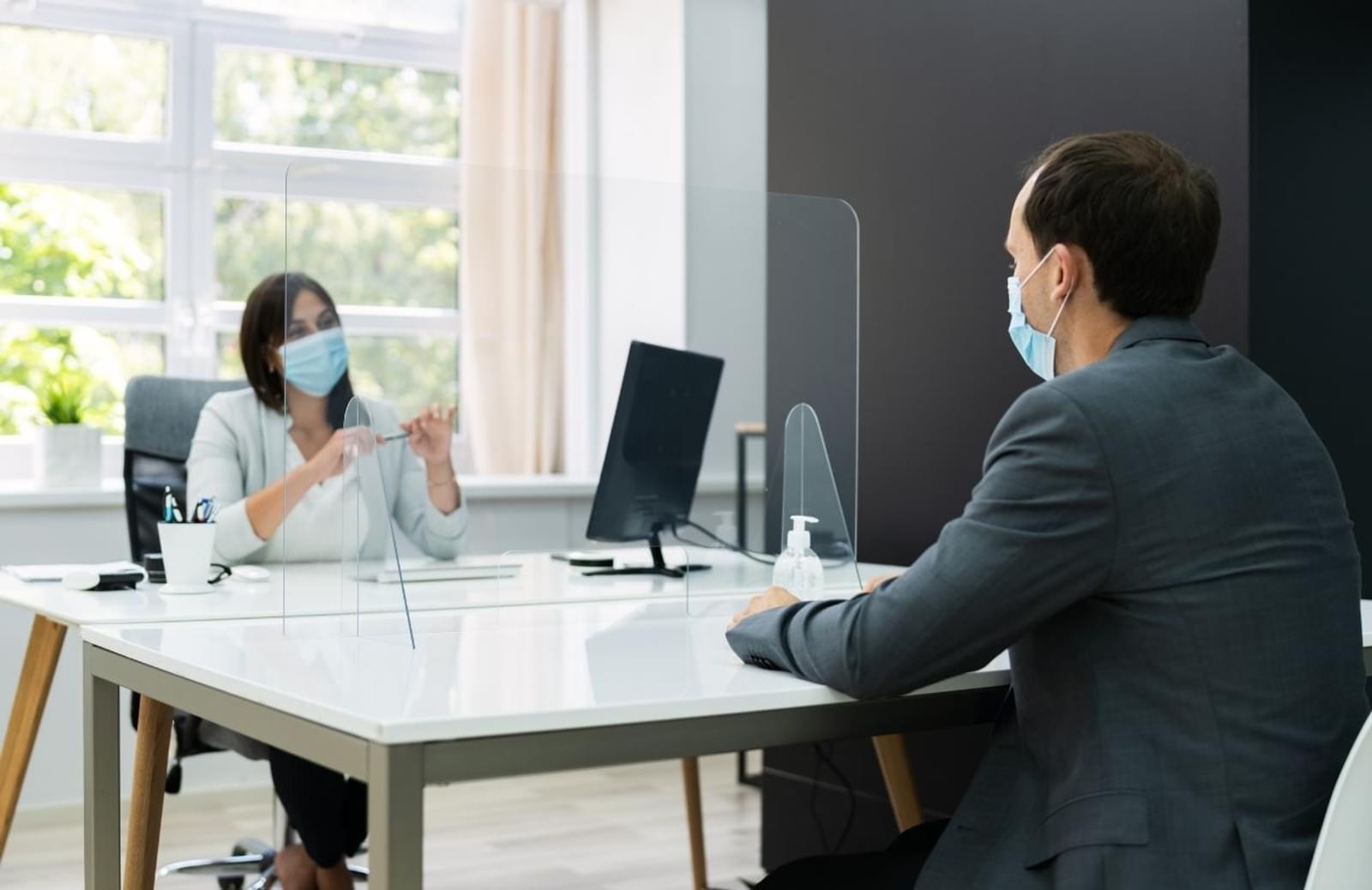 Woman and man sitting across a table from each other wearing medical masks