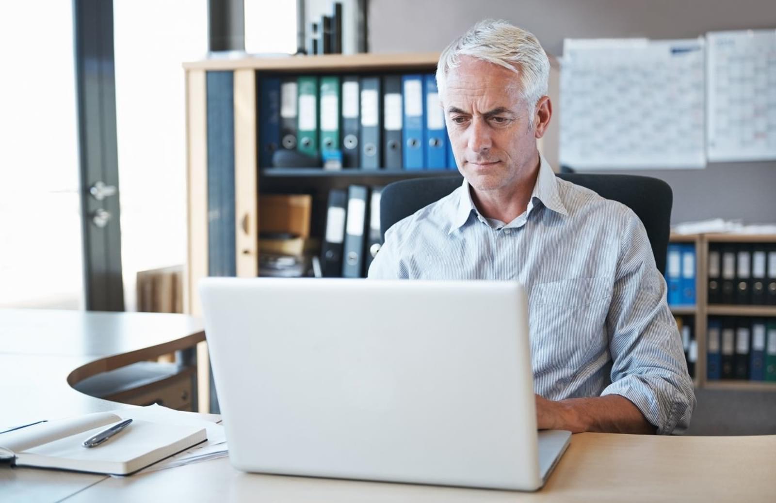 Gray-haired man sitting at desk working on a laptop computer