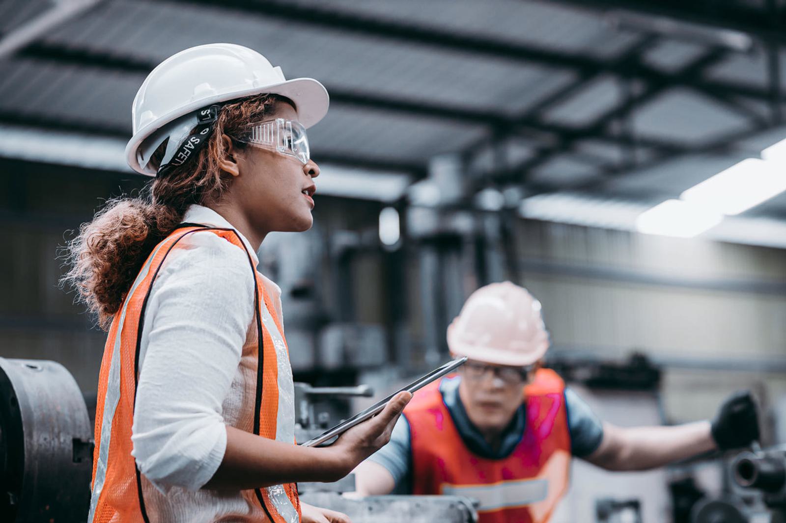 Two woman wearing hardhats while working in industrial setting