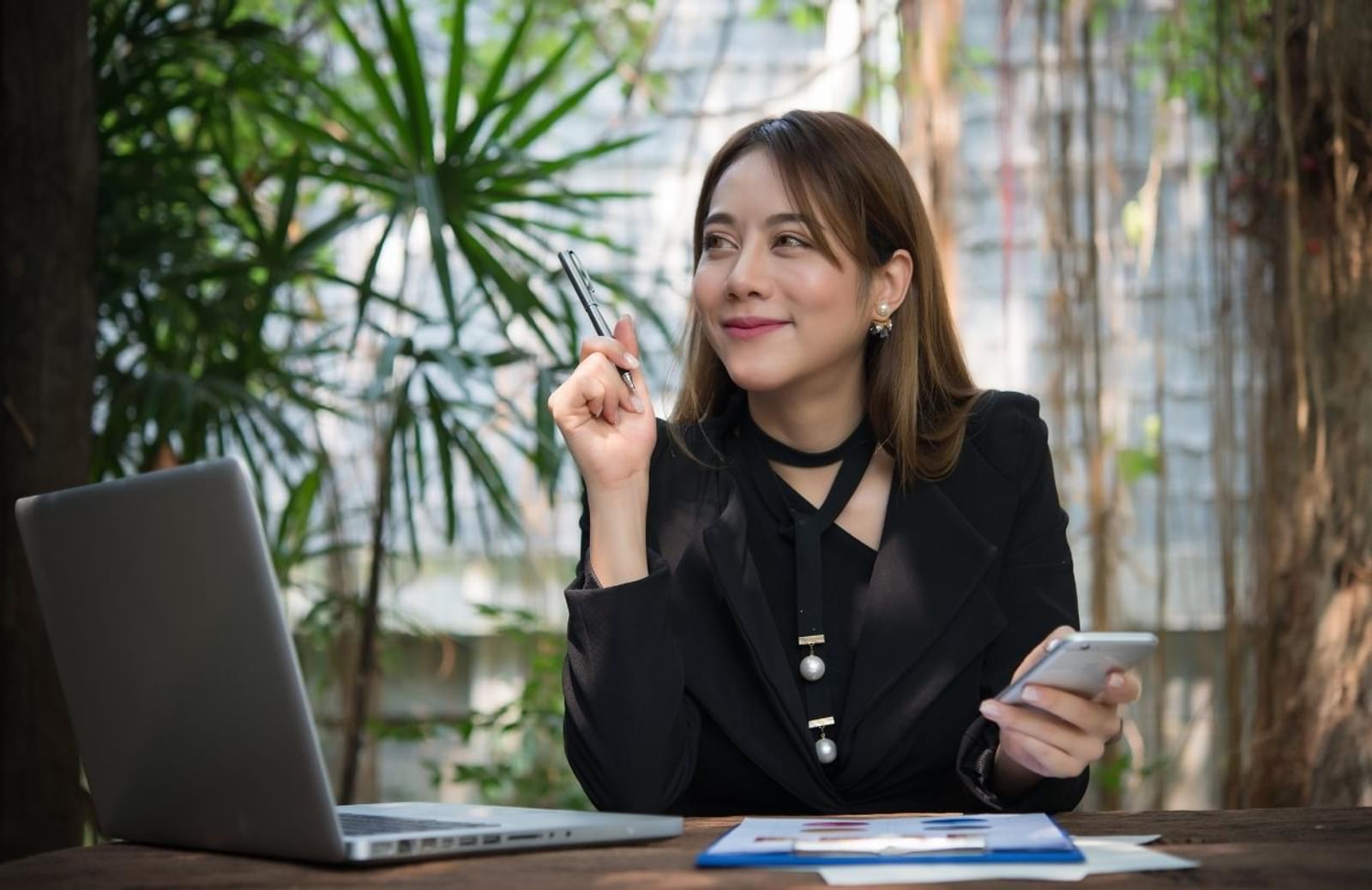 Woman at desk holding cellphone with open laptop
