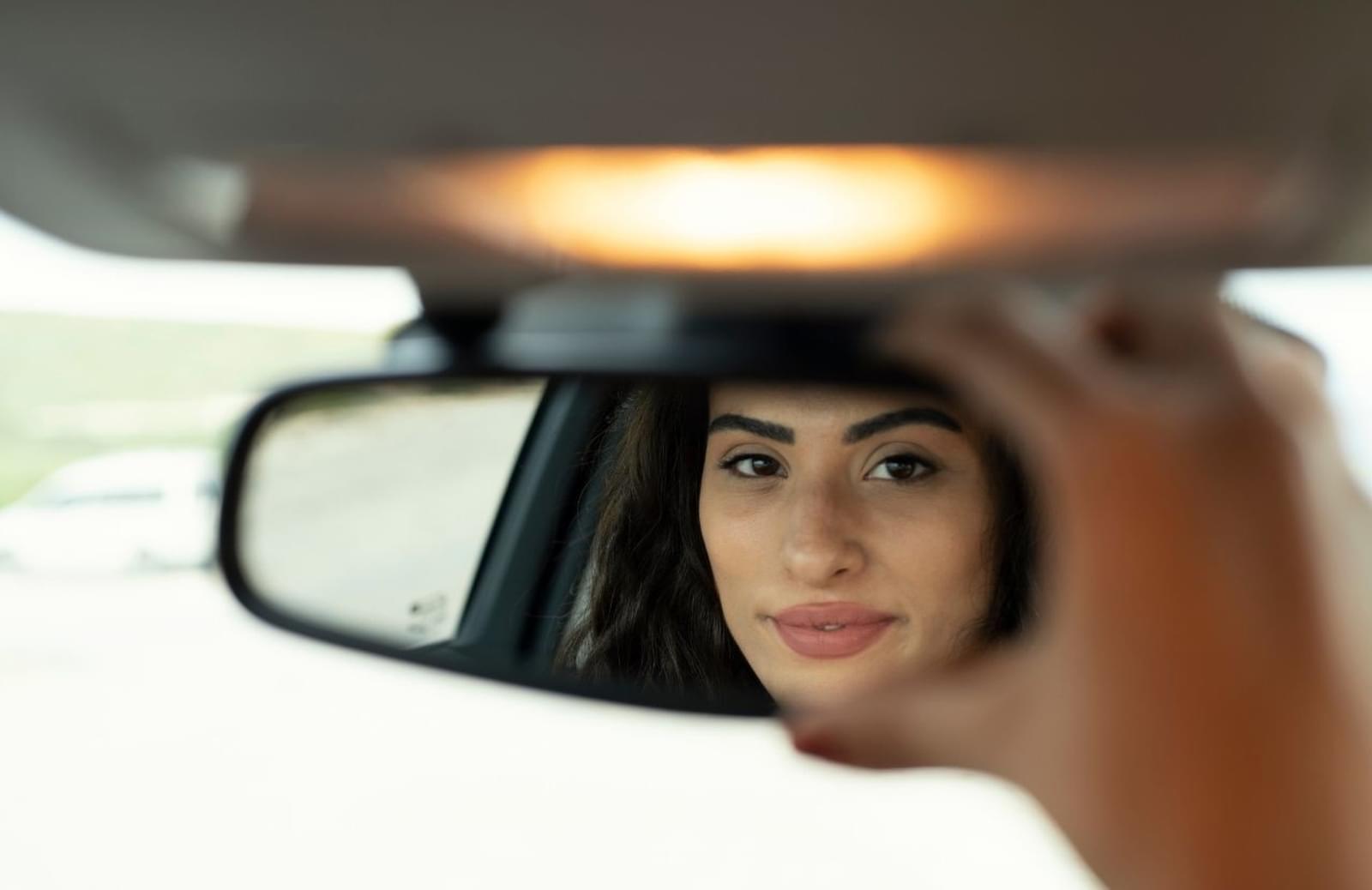 Woman smiling to herself as she adjusts rearview mirror in car