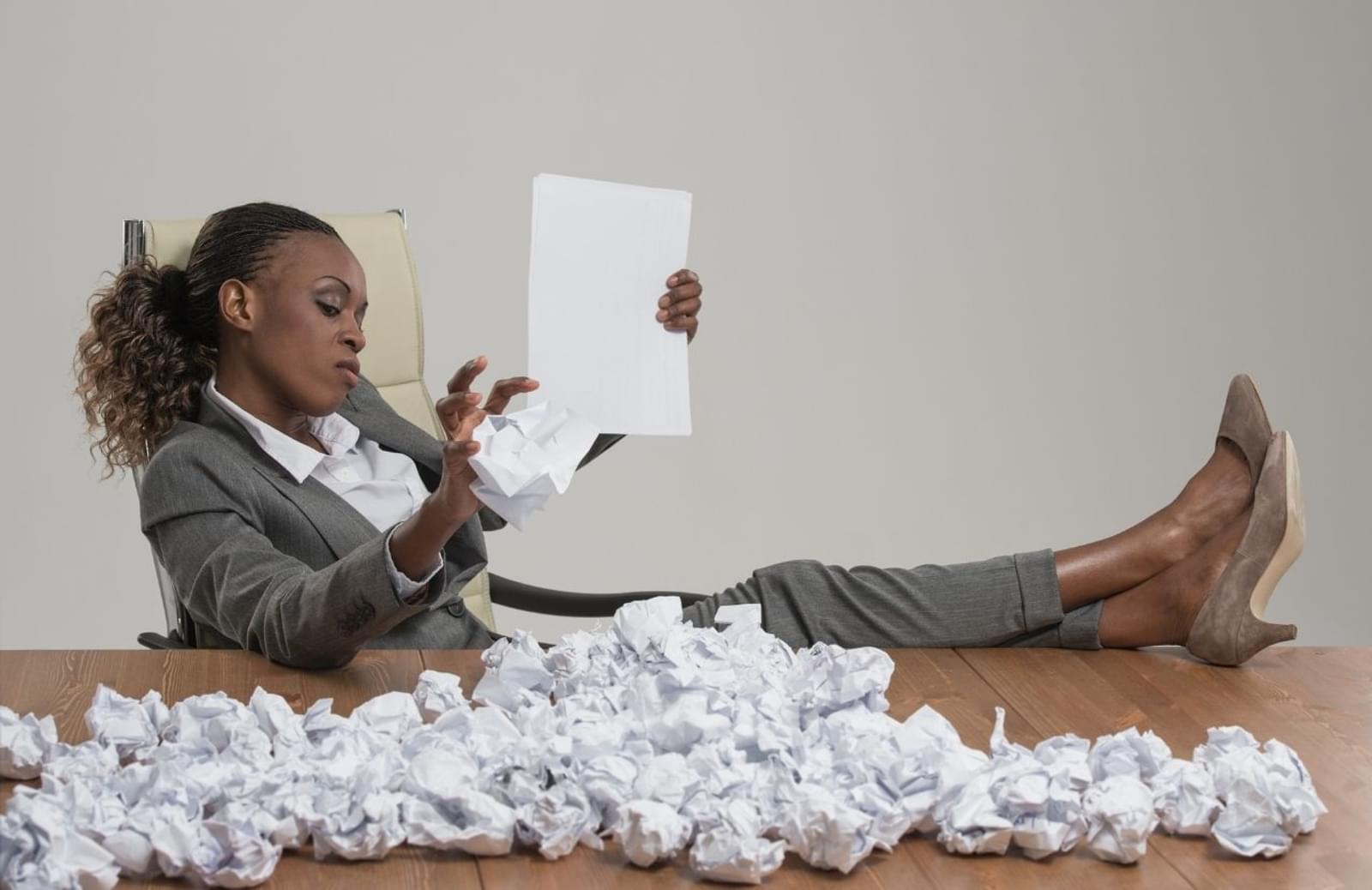 Business woman sitting with feet up on desk covered with balled-up paper