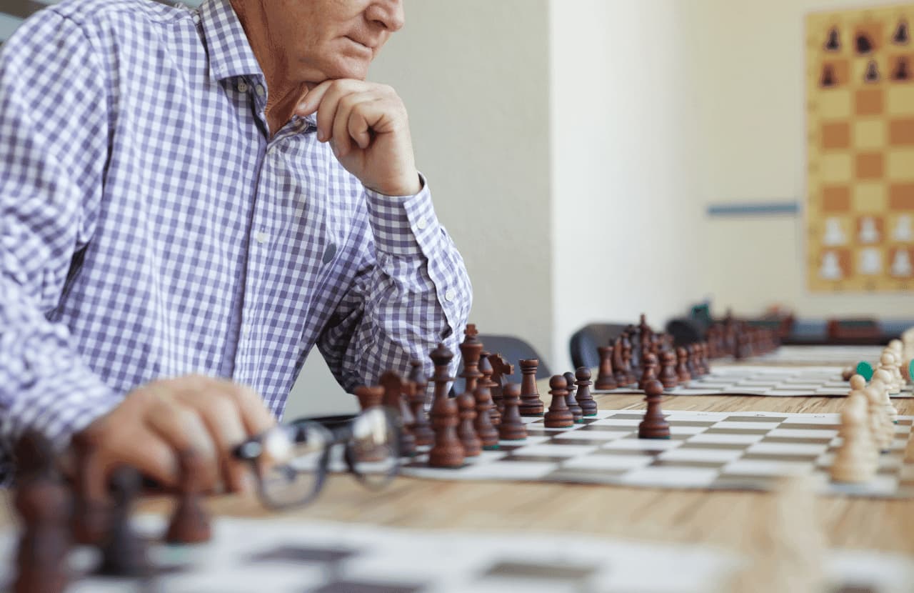 A man in a checkered shirt contemplates his next move on the chess board in front of him