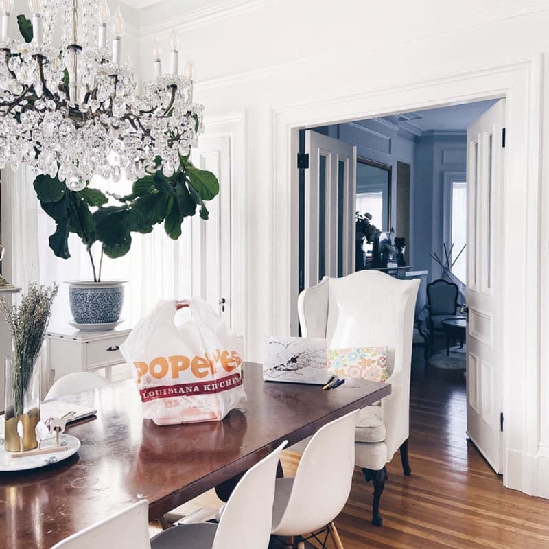 Kellie Van's beautifully white dining room with a crystal chandelier and a bag of Popeyes takeout on the wooden table