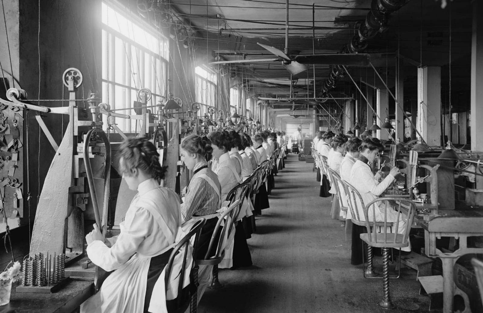 Vintage image of women in workshop assembly line sewing on antique machines