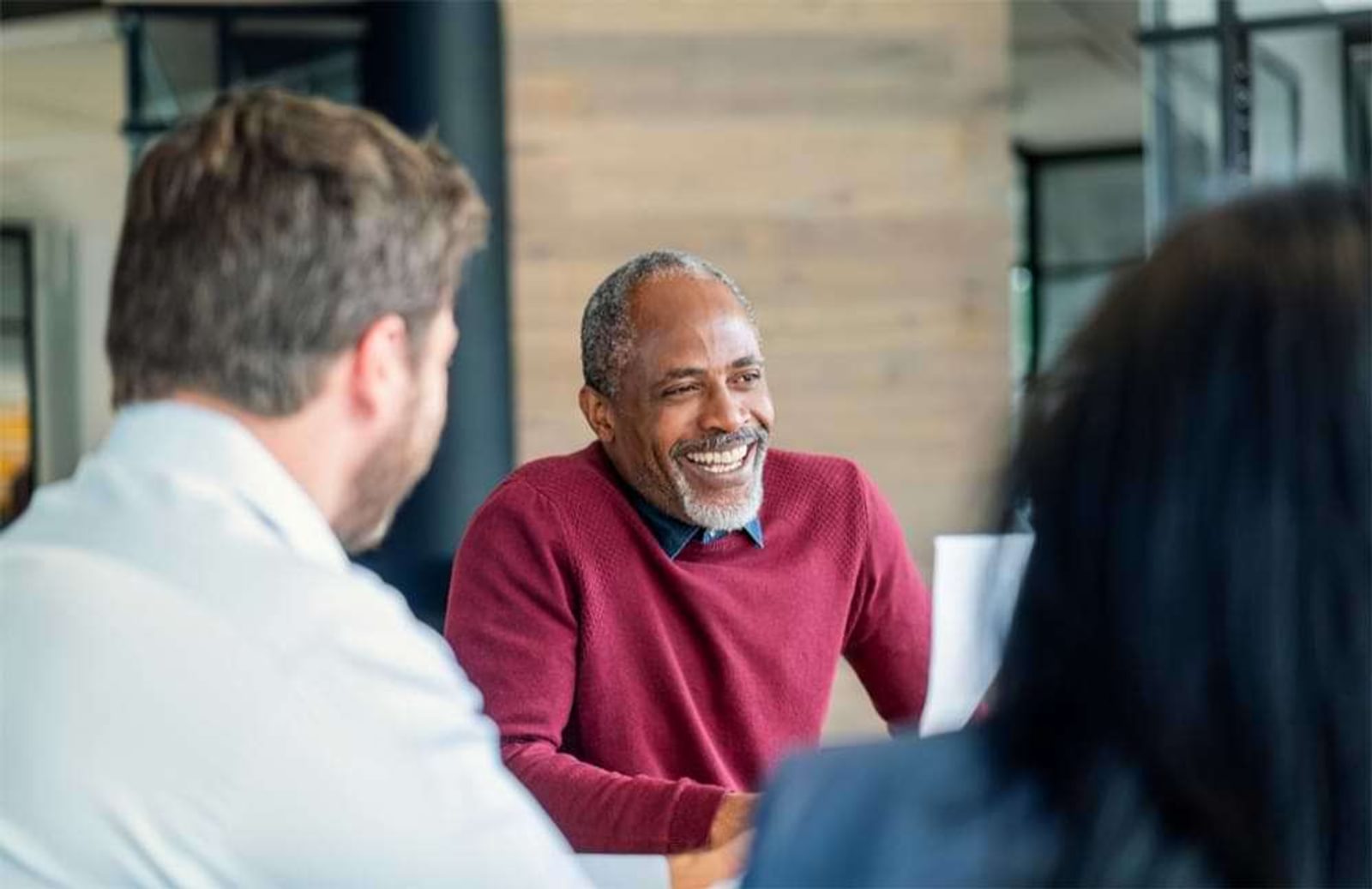 Mature man in red sweater laughing at colleagues in office