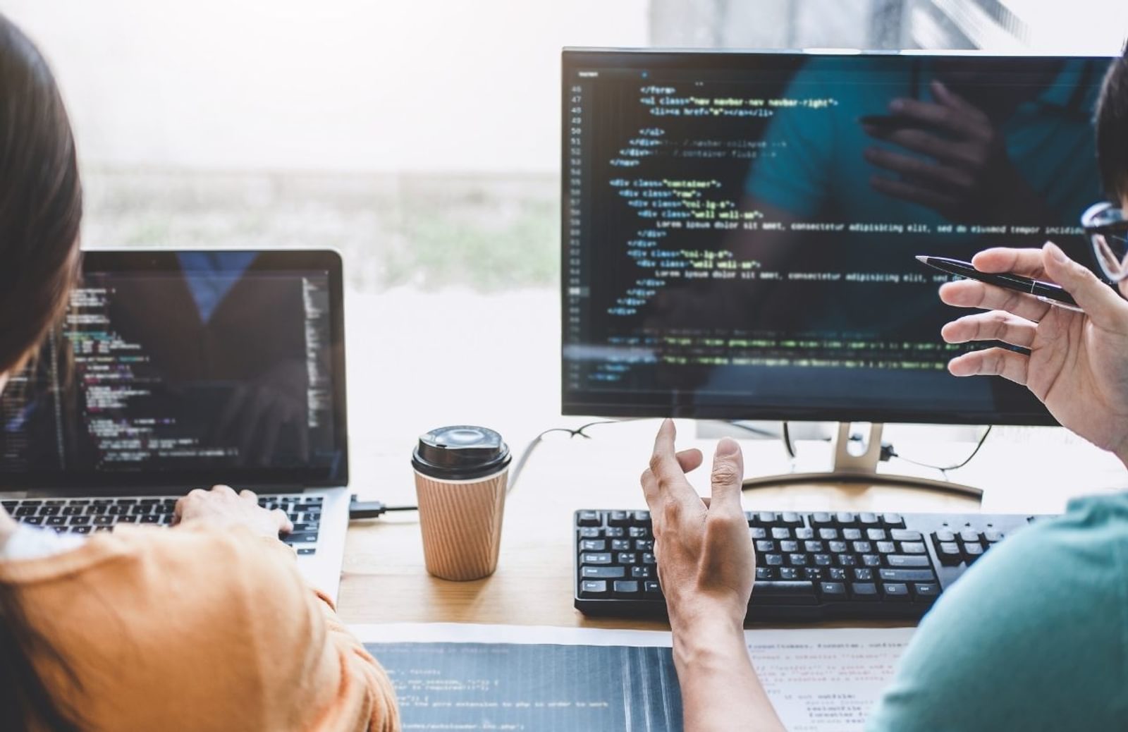 Two people seen from back while working on coding at computer screens