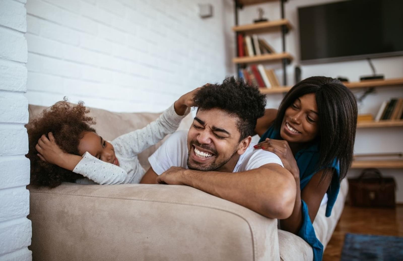 Young family laughing and cuddling on sofa