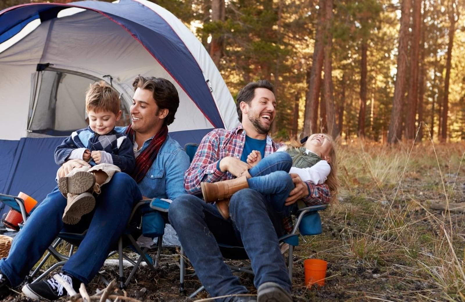Two adults holding their children while sitting in front of tent at campsite