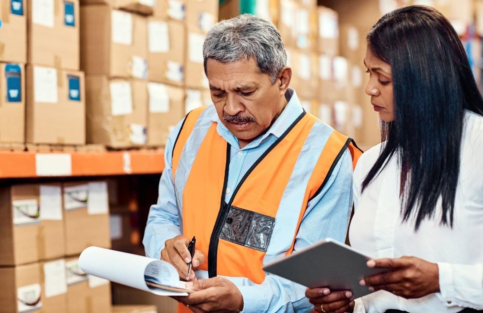 Warehouse man and woman holding tablet and paper and discussing their contents