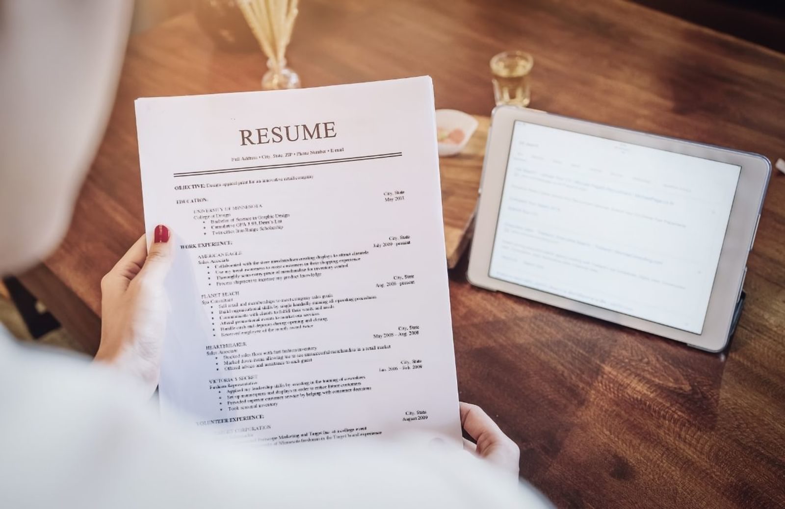 Person holding resume over desk with tablet