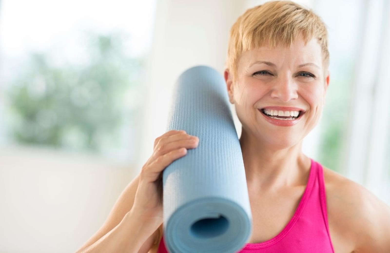 Smiling woman holding rolled-up yoga mat