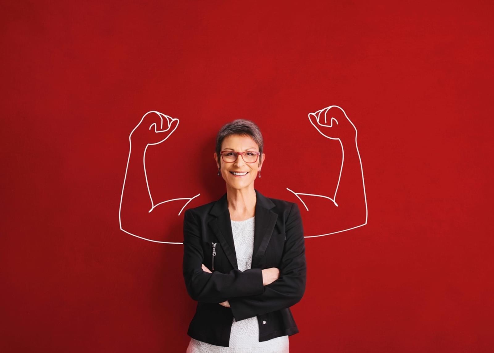 Woman standing with arms crossed in front of a red wall with chalk arms and biceps behind her