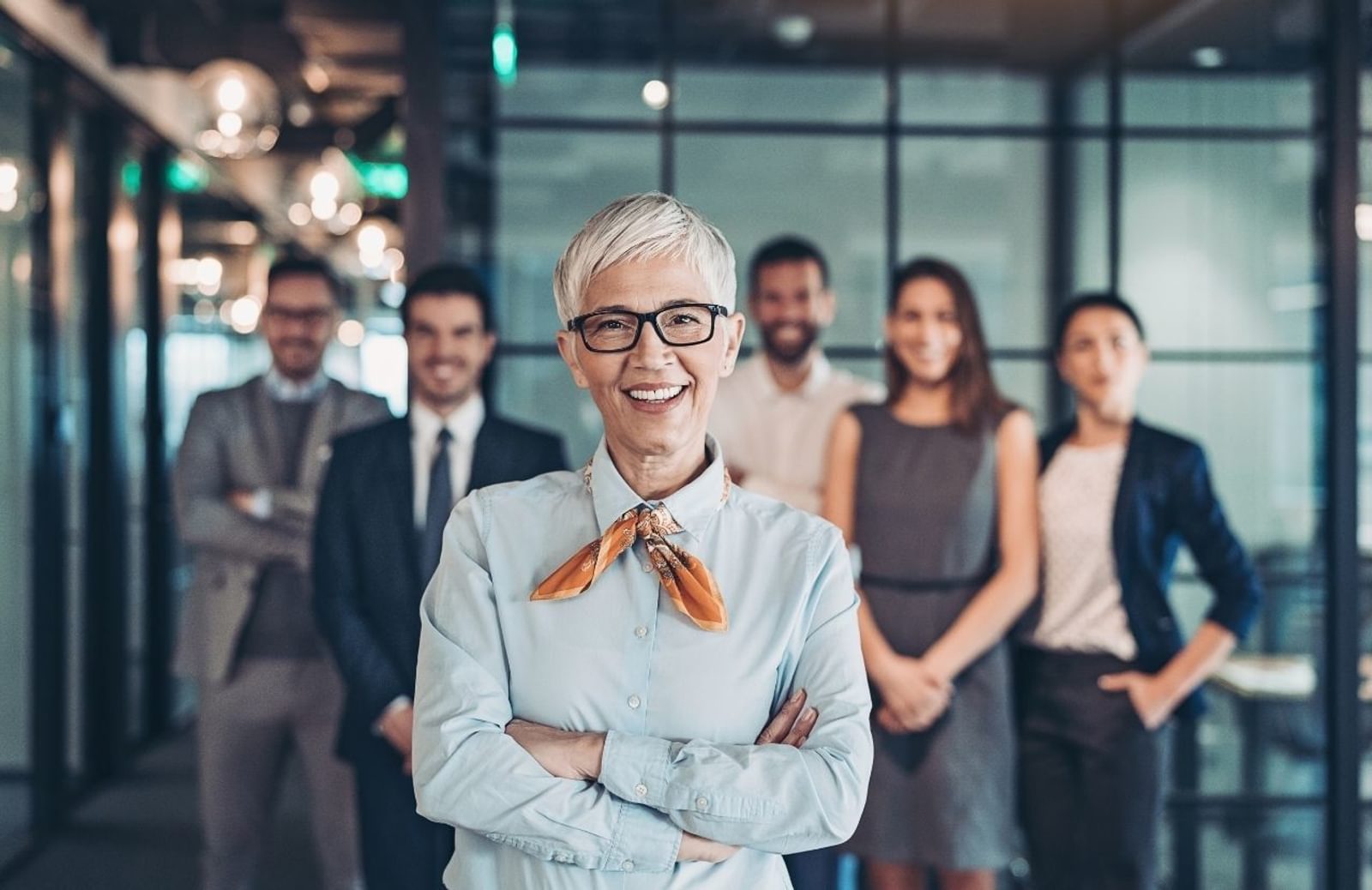 Smiling mature woman in office with coworkers in line behind her at work