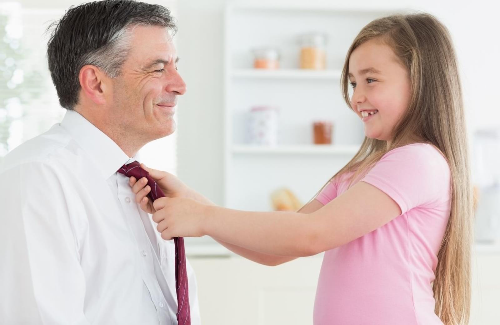 Professional man smiling while young daughter ties his tie