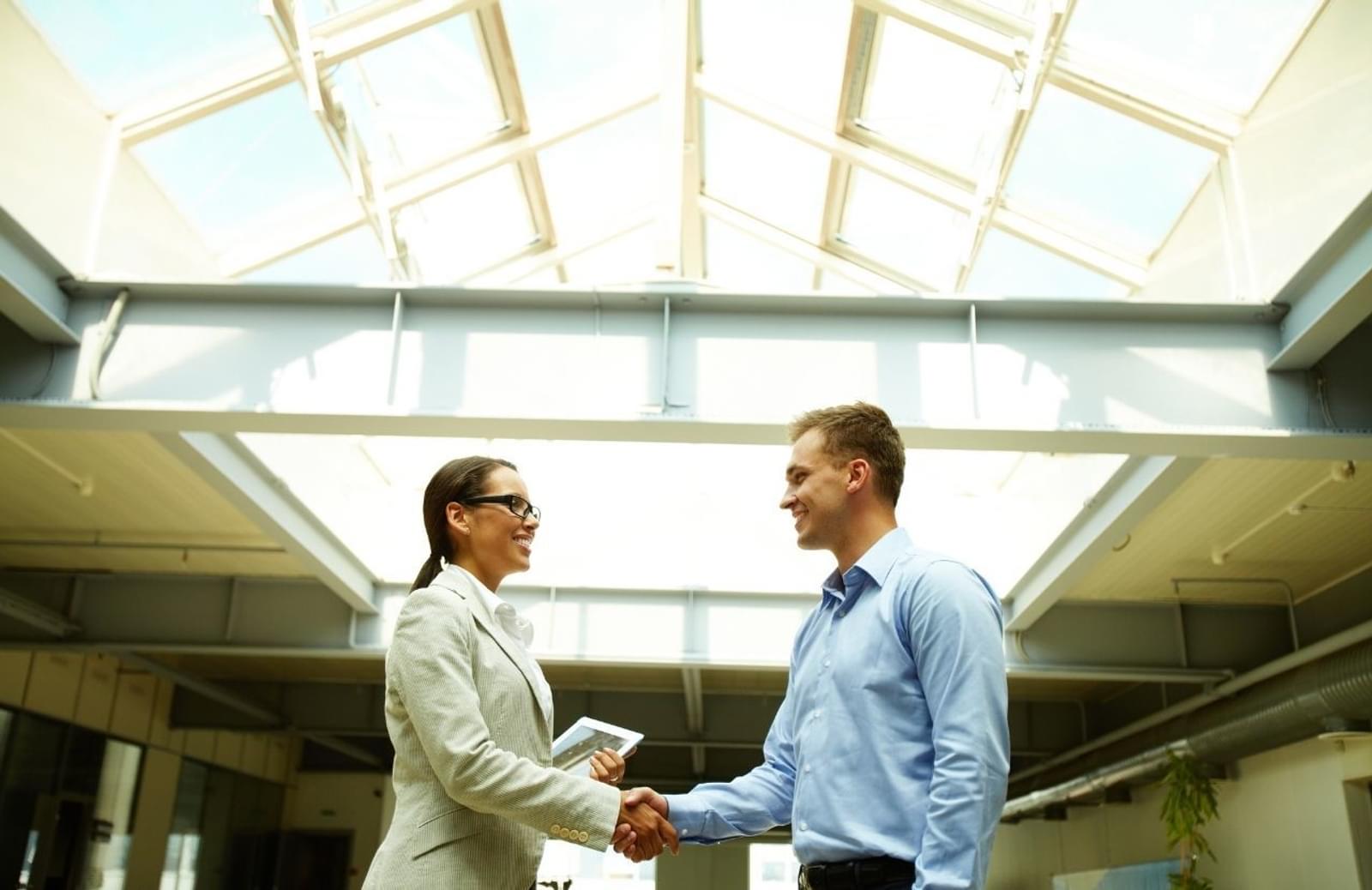 Two professionals shaking hands while standing in glass-covered hallway