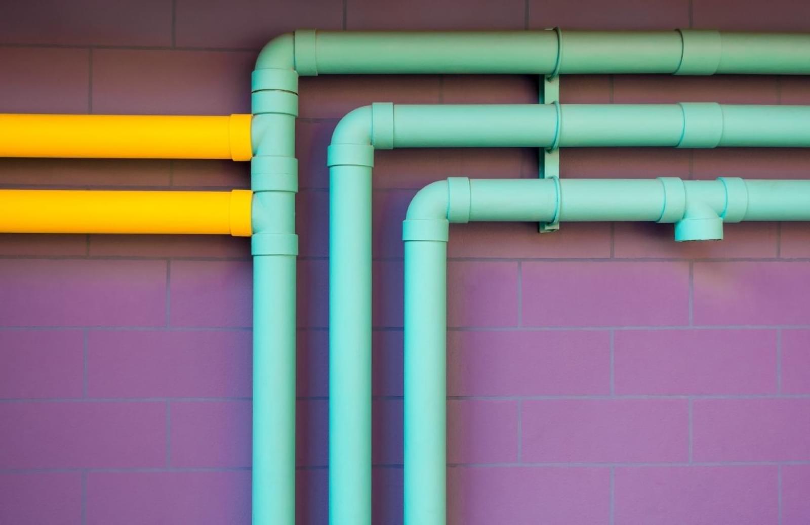 Teal and yellow pipelines against purple brick wall