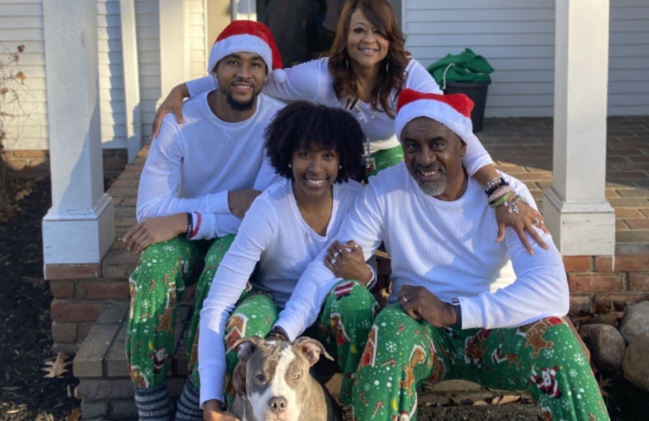 Janet and her family in long white sleeved t-shirts and green candy cane pajama bottoms. Janet's son and her husband are wearing Santa hats. Her husband and daughter are holding their grey and white pit bull dog.