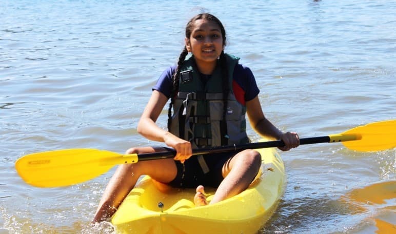 Sandhiya's daughter paddles through a lake on a yellow kayak