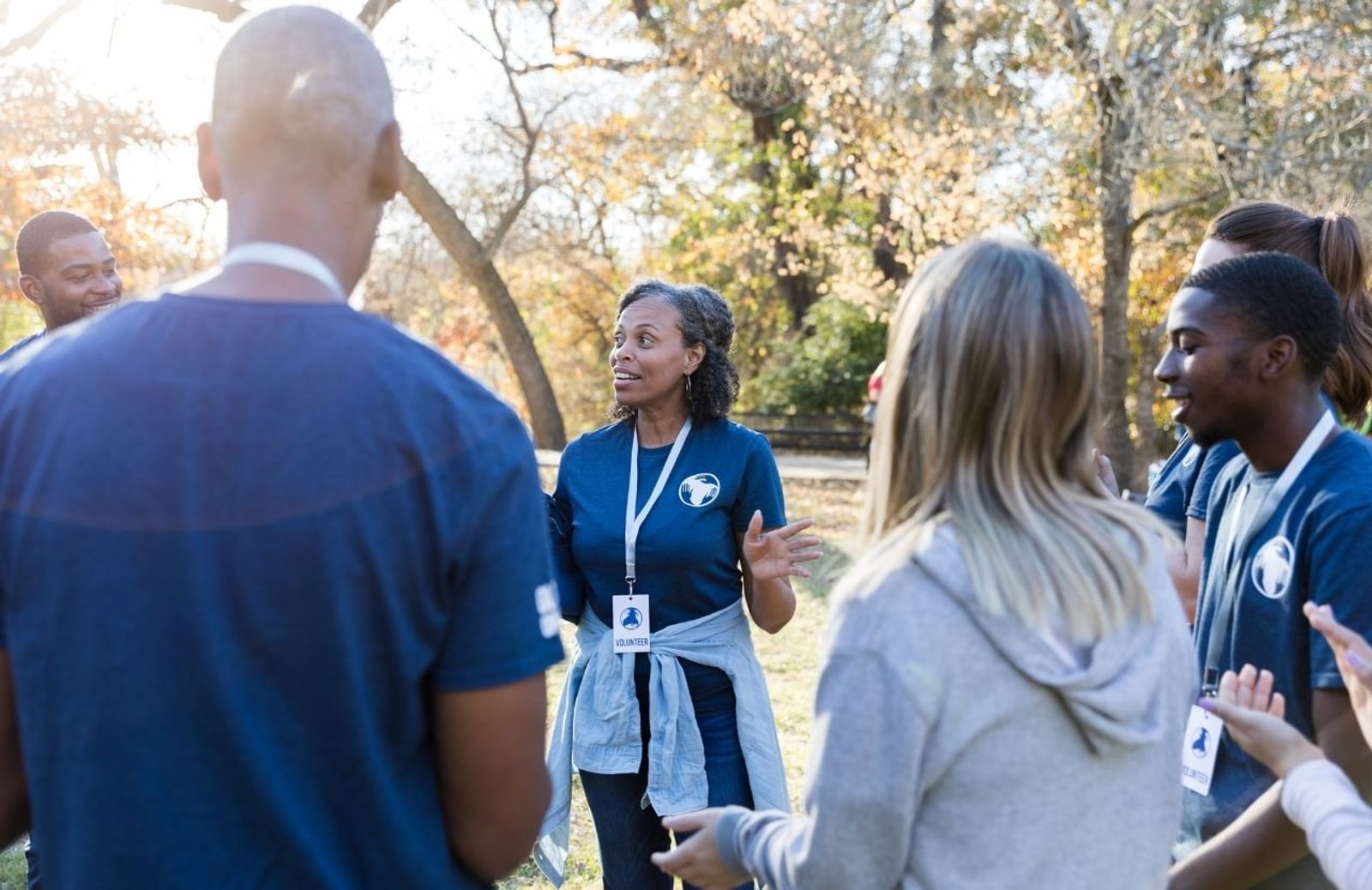 Group of people standing in a circle outside while one person talks to them