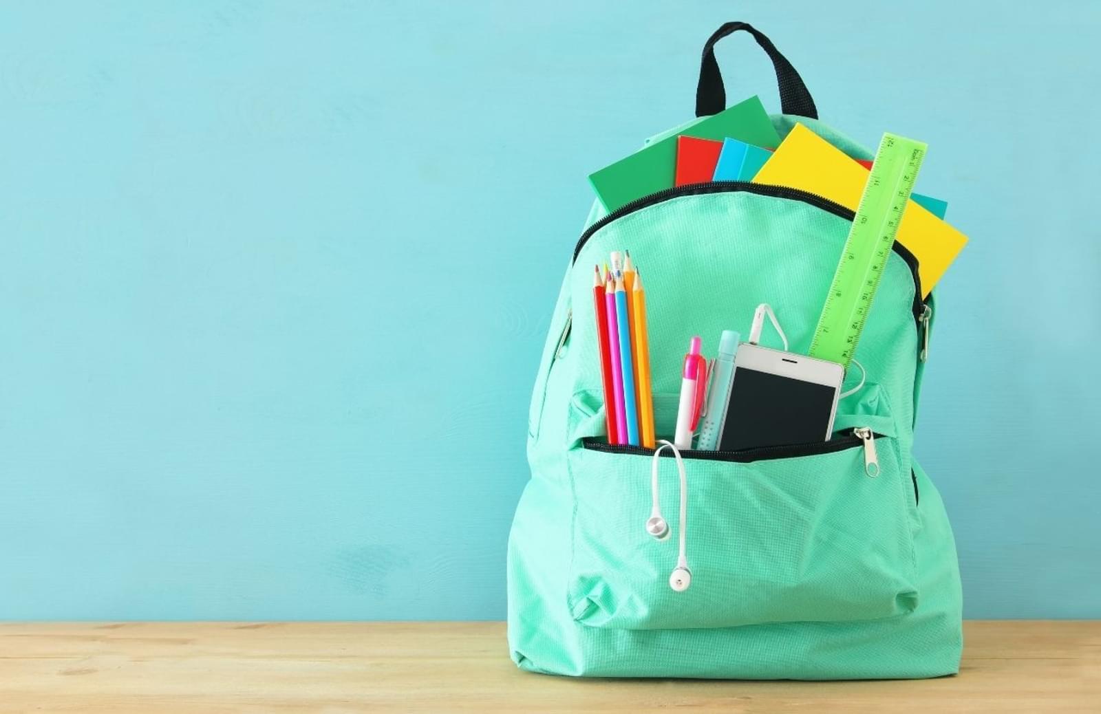 Green backpack filled with school supplies on desk